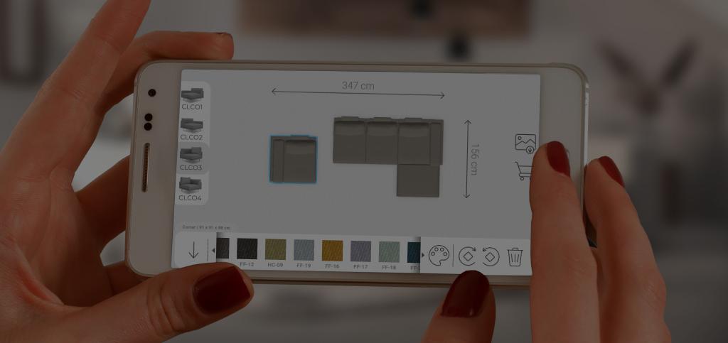 Una mano tiene un telefono con il configuratore FEYDOM, sullo schermo un divano configurato con le misure